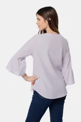 Blusa de lino color lila, con cuello redondo y mangas tres cuartos que finalizan en volados amplios. Presenta un diseño liso y cierre frontal con botones metálicos.
