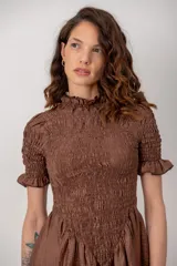 Vestido corto color marrón chocolate, con cuerpo fruncido tipo nido de abejas, cuello alto con volados y mangas cortas abuchonadas con terminación en volado. Presenta falda evasé con vuelo.
