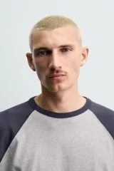 Camiseta de corte relajado con diseño color block, cuerpo en gris melange y mangas largas raglán en color azul marino. Presenta cuello redondo al tono de las mangas y bajo con acabado irregular.