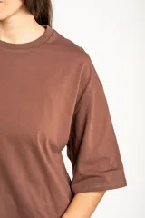 Remera oversize marrón con corte a la altura de la cadera, cuello redondo y mangas cortas holgadas. Incorpora un aplique inferior superpuesto de satén con detalles de encaje bordado en los bordes.