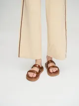 Sandalias de cuero vacuno color marrón con acabado brillante, diseño de dos tiras anchas acolchadas y plataforma baja.
