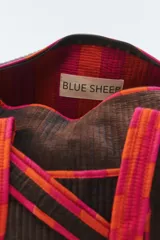 Bolso de viaje tipo duffel de color gris oscuro, confeccionado en algodón acolchado con pespuntes verticales. Cuenta con asas de mano y una correa larga regulable con detalles de tiras en tonos fucsia y naranja, cierre superior y herrajes metálicos dorados.