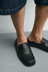 Mocasín destalonado de cuero negro con detalle de antifaz en el empeine, puntera cuadrada y suela plana con pequeño tacón.