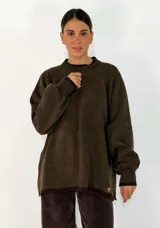 Sweater de tejido de punto en color verde militar, con cuello redondo, mangas largas con puños acanalados y diseño holgado. Presenta un pequeño detalle metálico en el ruedo.