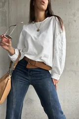 Blusa blanca de lino con mangas largas abullonadas, destacada por paneles laterales bordados con detalles de encaje. Presenta un corte holgado y cuello redondo.