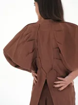 Camisa de lino blanca, de corte oversize, con mangas largas abullonadas, cuello mao y botones. Es más larga en la parte trasera e incluye un tajo en la espalda.