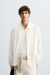 Camisa de corte relajado, color blanco hueso, con finas rayas verticales en tono grisáceo. Presenta cuello solapa, manga larga, bolsillo de parche en el pecho y bajo con aberturas laterales.