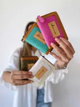 Billetera compacta de cuero con diseño bicolor en turquesa y marrón, con textura tipo reptil. Cuenta con cierre metálico perimetral y parche frontal con el logo de la marca.