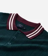 Polo de manga corta confeccionado en tejido de punto texturizado con trama vertical. Presenta cuello, puños y ruedo en color bordó con detalles de rayas blancas en contraste. Cuenta con una abertura frontal con tres botones.