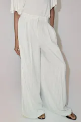 Pantalón wide leg de tiro medio, color blanco con diseño de rayas diplomáticas a contraste, bolsillos laterales y de vivo en la espalda, pinzas en el delantero y cierre frontal con cremallera, botón y ganchos metálicos.