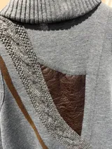 Chaleco de lana merino color gris, sin mangas, con cuello chal tejido en rib, bolsillos frontales applicados con ribete de cuero y cierre de botones tipo duffle con presillas de cuero.