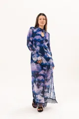 Vestido largo de manga larga con terminación campana, de color azul y violeta con estampado tie-dye, cuello mao con ojal y tajo frontal. Cuenta con flecos en el ruedo y tajo en la pierna.