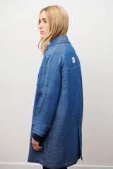 Spolverino largo de jean color azul, con cuello camisero, botones frontales y costuras decorativas en blanco.