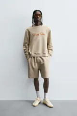 Sudadera de algodón color beige claro, corte relajado, cuello redondo y manga larga. Presenta bordado en relieve en el frente con texto en cursiva de color cobre.