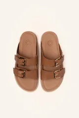 Sandalias de cuero color negro con dos tiras anchas sobre el empeine, cada una con hebillas metálicas ajustables y detalles de tachas plateadas. La suela es de cuero con un borde de color madera.