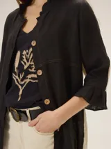 Camisa de lino de silueta relajada y largo irregular, color beige, con cuello mao, botones frontales a contratono y mangas tres cuartos terminadas en volados.