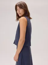 Chaleco negro sin mangas, de corte recto y largo a la cintura, con cuello redondo y cierre frontal oculto.