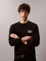 Buzo Calvin Klein de felpa color negro, con cuello redondo, manga larga, puños y dobladillo acanalados. Presenta un bordado frontal con la palabra "VERY" en tonos verdosos y debajo el logo de la marca.