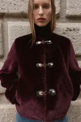 Chaqueta de cuello redondo y manga larga con tejido exterior efecto pelo e interior efecto ante. Presenta bolsillos delanteros de vivo y cierre frontal con alamares metálicos.