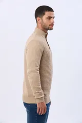 Buzo de punto color beige, con cuello alto y cierre frontal con cremallera y solapa de gamuza con botón. Presenta un tejido texturizado en el cuerpo y mangas lisas.