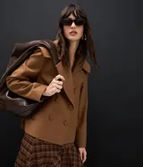Campera pesada de estructura firme, color marrón, con cuello amplio de solapa alargada, cierre cruzado con botones, mangas largas y bolsillos delanteros. Presenta un canesú sobrepuesto en la espalda con pliegue central.