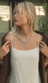 Collar artesanal de piedras naturales de aguamarina en tonos celestes, con dije colgante en forma de pez de acero y cierre metálico.