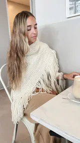 Ruana tejida a mano en lana merino, de color negro, con diseño de textura tejida y terminaciones con flecos largos en todo el borde.