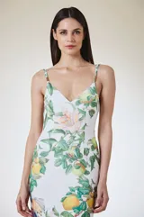Vestido largo de silueta fluida con estampado botánico de frutas y flores sobre fondo blanco. Presenta escote en V y breteles finos con detalles metálicos.