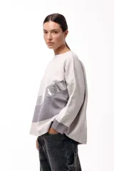 Sweater de punto con diseño de bloques de color en diagonal, combinando negro, beige y una franja central con textura metalizada. Presenta cuello redondo, mangas largas con puños en contraste y un corte holgado.