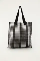 Bolsa tote de diseño amplio a rayas verticales en blanco y negro, con asas de hombro negras y aplique frontal bordado con letras.