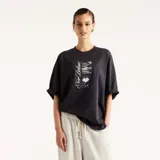 Remera oversize de color negro, confeccionada en algodón, con cuello redondo y mangas cortas. Presenta un estampado gráfico frontal con diseño abstracto en blanco y negro y la inscripción "New Balance".