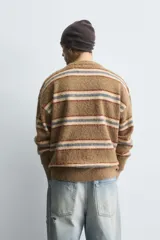 Jersey de corte relajado con acabado cepillado, cuello redondo y manga larga. Presenta un diseño de rayas horizontales en tonos tierra, azul y crema con acabados en rib.