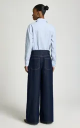 Jean wide leg de tiro alto color azul oscuro, con bolsillos delanteros curvos, bolsillos traseros y cierre frontal de cremallera y botón con pespuntes en contraste.