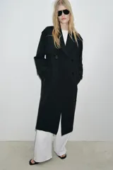 Trench largo de color negro con cuello de solapa, manga larga con trabillas ajustables y cierre frontal cruzado con doble botonadura. Cuenta con bolsillos delanteros de vivo, solapa cortavientos en el pecho y cinturón ajustable del mismo tejido.