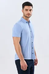 Camisa de piqué lisa color celeste, de manga corta, con cuello camisero y cierre frontal de botones oscuros.