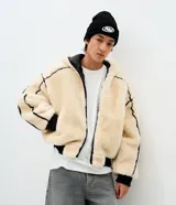 Campera de fleece color beige con diseño de paneles, costuras expuestas en color negro y cierre frontal. Posee cuello alto, mangas largas con puños elásticos y forro interior.