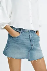 Falda pantalón de denim azul con diseño de cinco bolsillos, cierre frontal con cremallera y botón, y bajo deshilachado sin costuras.