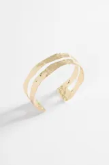 Brazalete rígido de diseño abierto con doble banda y acabado texturizado martillado en tono dorado.