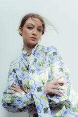 Camisa blanca con estampado de flores azules y verdes, cuello con lazo y mangas largas abullonadas.