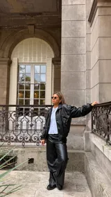 Campera de cuero sintético color negro, con cuello camisero, cierre frontal y costuras visibles en contraste. Presenta un diseño holgado con puños elásticos.