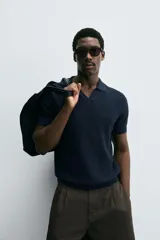 Polo de manga corta, color celeste pálido, con cuello solapa y abertura frontal en V. Tejido de punto con textura acanalada vertical.