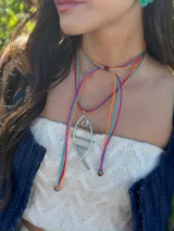 Collar con tres tientos sintéticos de colores fucsia, celeste y naranja, con medallón plateado en forma de pez hecho de alambre.