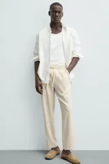 Pantalón de corte relajado color beige confeccionado en tejido de mezcla de algodón y lino. Posee cintura elástica ajustable con cordón, bolsillos frontales y bolsillos traseros de vivo.