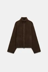 Chaqueta de punto marrón de textura bouclé, con cuello subido, manga larga ancha y cierre frontal oculto con cremallera.