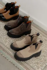 Bota tipo chelsea de punta redonda, confeccionada en una combinación de cuero texturizado y gamuza en tonos marrones. Presenta elásticos laterales negros y una suela track robusta de goma negra.