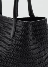 Bolso tipo tote negro confeccionado en cuero con diseño trenzado, asas largas para el hombro y cierre de botón magnético.