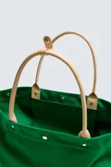 Bolso tipo shopper de tejido de algodón color verde, con asas de mano en piel color beige y cierre superior mediante botones a presión. Cuenta con compartimento principal amplio y bolsillos interiores.