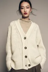 Chaqueta de punto de lana con cuello en pico, manga larga y cierre frontal con botones oscuros. Presenta un diseño de tejido grueso y holgado.