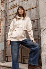 Gabardina liviana color beige con capucha, cierre frontal oculto y cintura ajustable mediante cordón. Presenta bolsillos delanteros amplios y mangas largas con puños rectos.