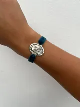 Pulsera con dije redondo dorado con la imagen de la Virgen de Fátima, sujetado por una banda elástica de terciopelo.